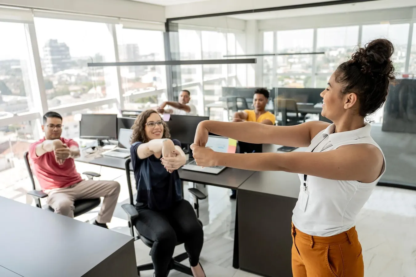 A group of diverse office workers performing guided arm and wrist stretches in a modern Singapore workspace to improve employee wellness and reduce desk-bound stiffness.